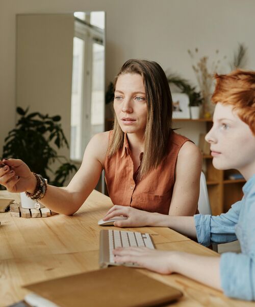 Eine Frau und ein Kind sitzen gemeinsam an einem Schreibtisch vor einem Computer und konzentrieren sich auf den Bildschirm.