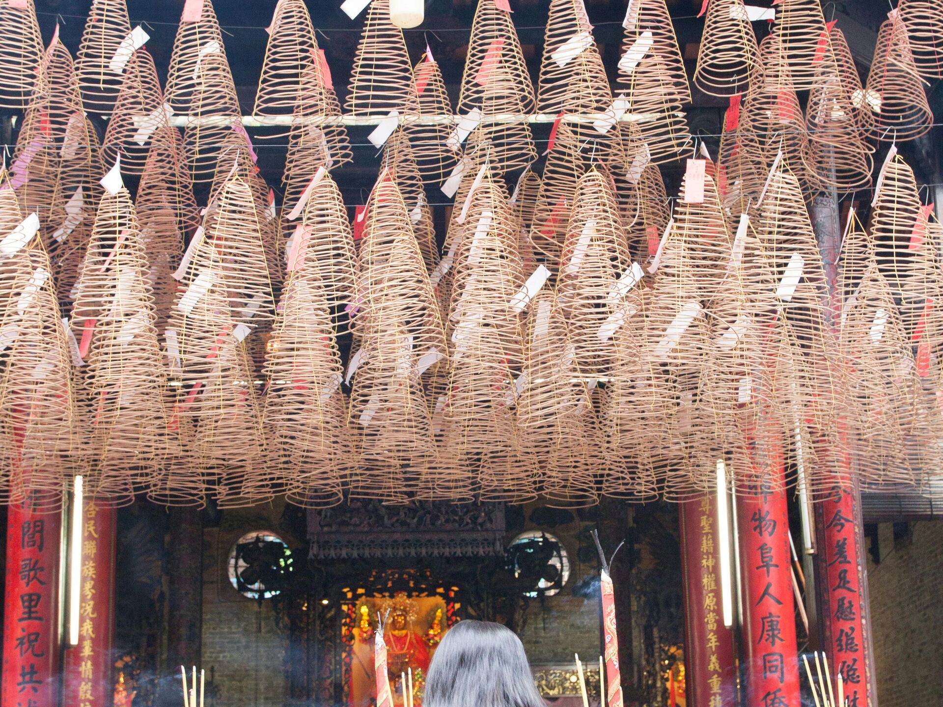 Eine Person steht in einem Tempel vor zahlreichen hängenden Räucherspiralen und brennenden Räucherstäbchen.