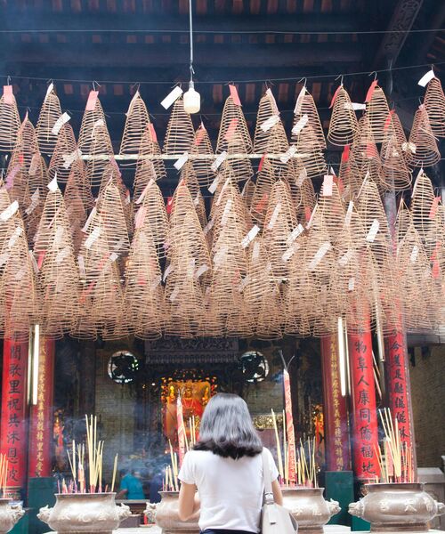 Eine Person steht in einem Tempel vor zahlreichen hängenden Räucherspiralen und brennenden Räucherstäbchen.