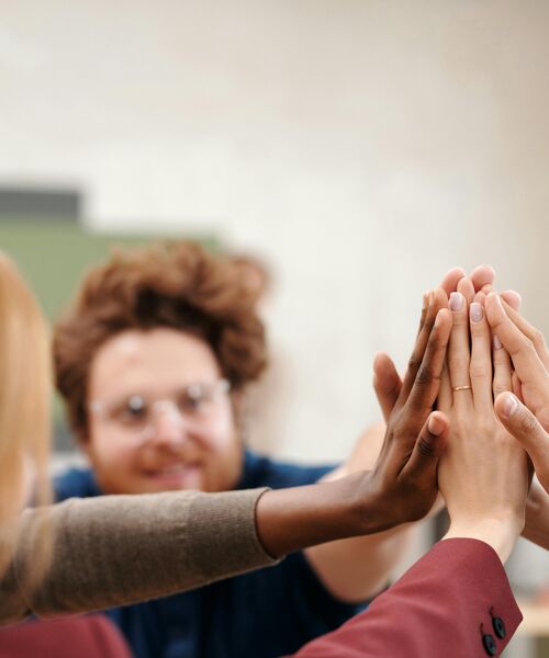 Mehrere Menschen geben sich ein gemeinsames High-Five als Zeichen für Teamgeist und Erfolg.