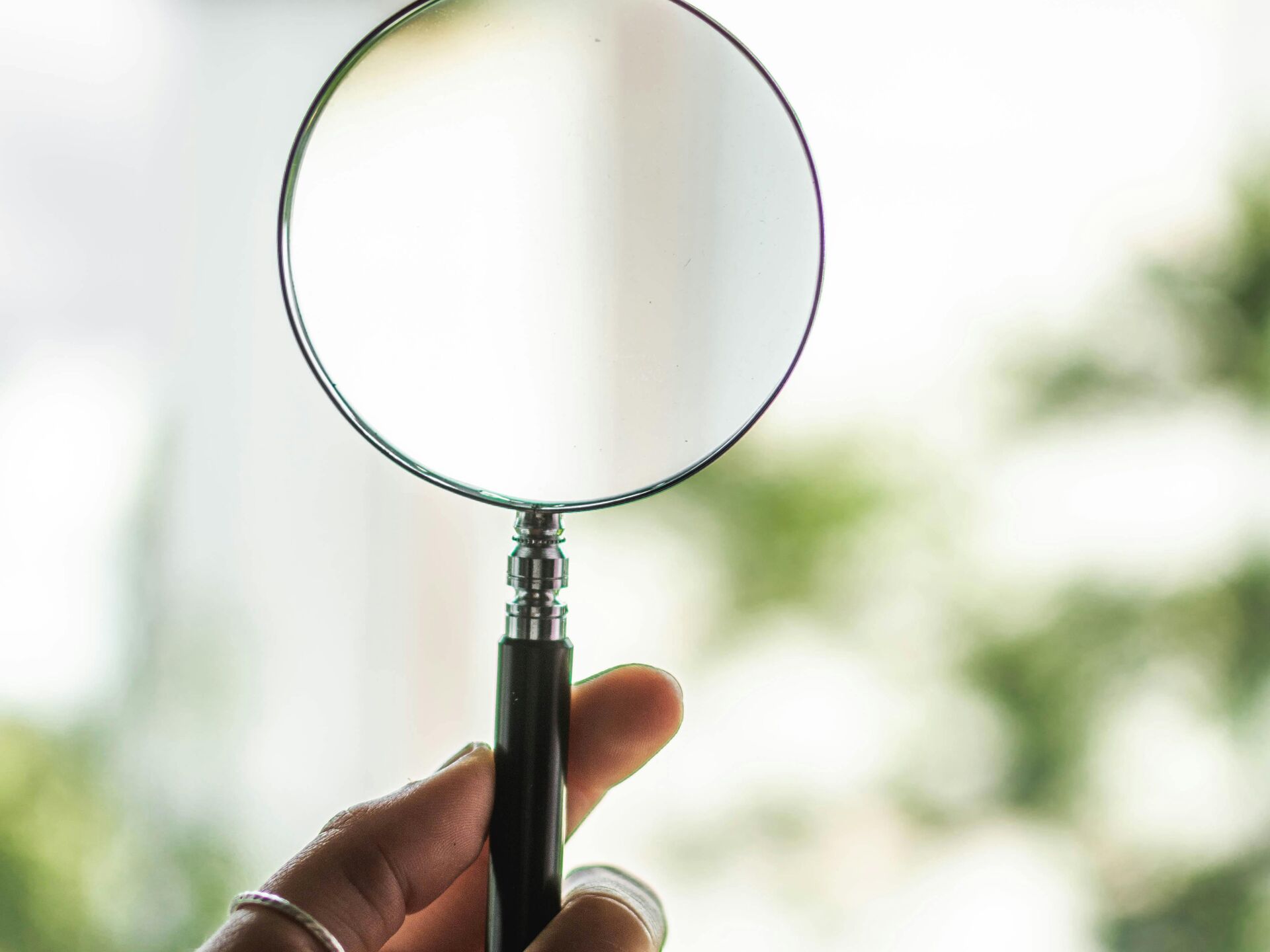 Eine Hand hält eine Lupe vor einem hellen, grünen Hintergrund ins Licht.