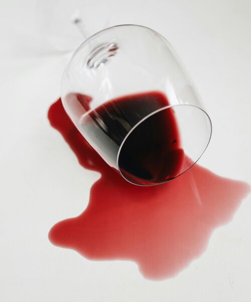 Ein umgekipptes Weinglas mit verschüttetem Rotwein auf einer hellen Oberfläche.