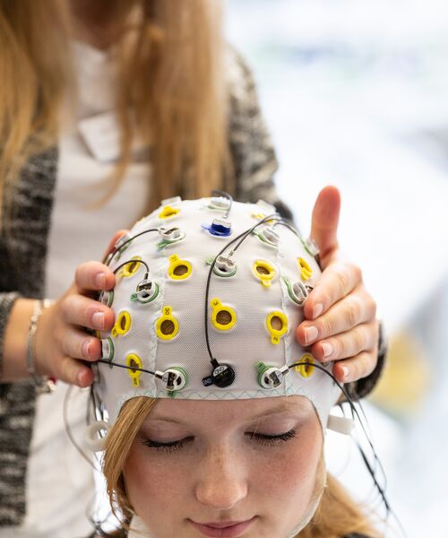 Person trägt eine EEG-Messhaube mit Elektroden, eine zweite Person justiert sie behutsam.