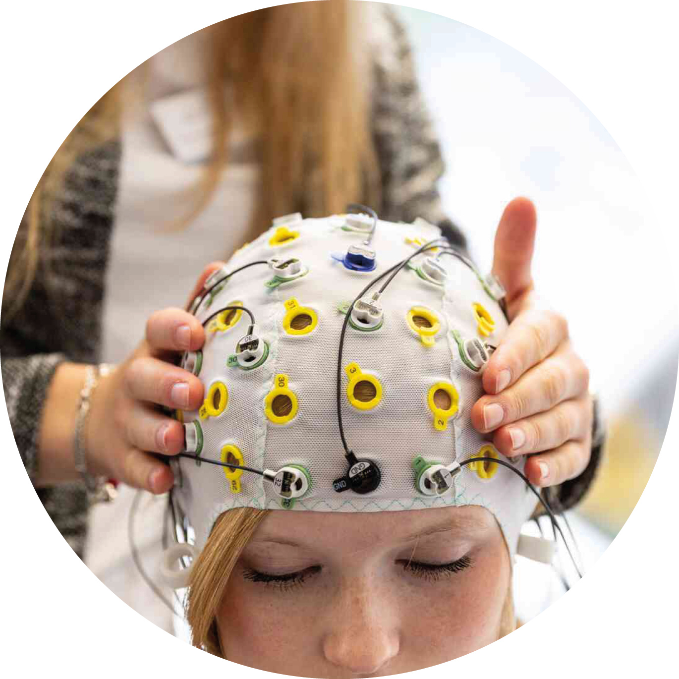 Eine Person trägt eine EEG-Messhaube mit Elektroden, während eine andere Person die Haube sorgfältig justiert.
