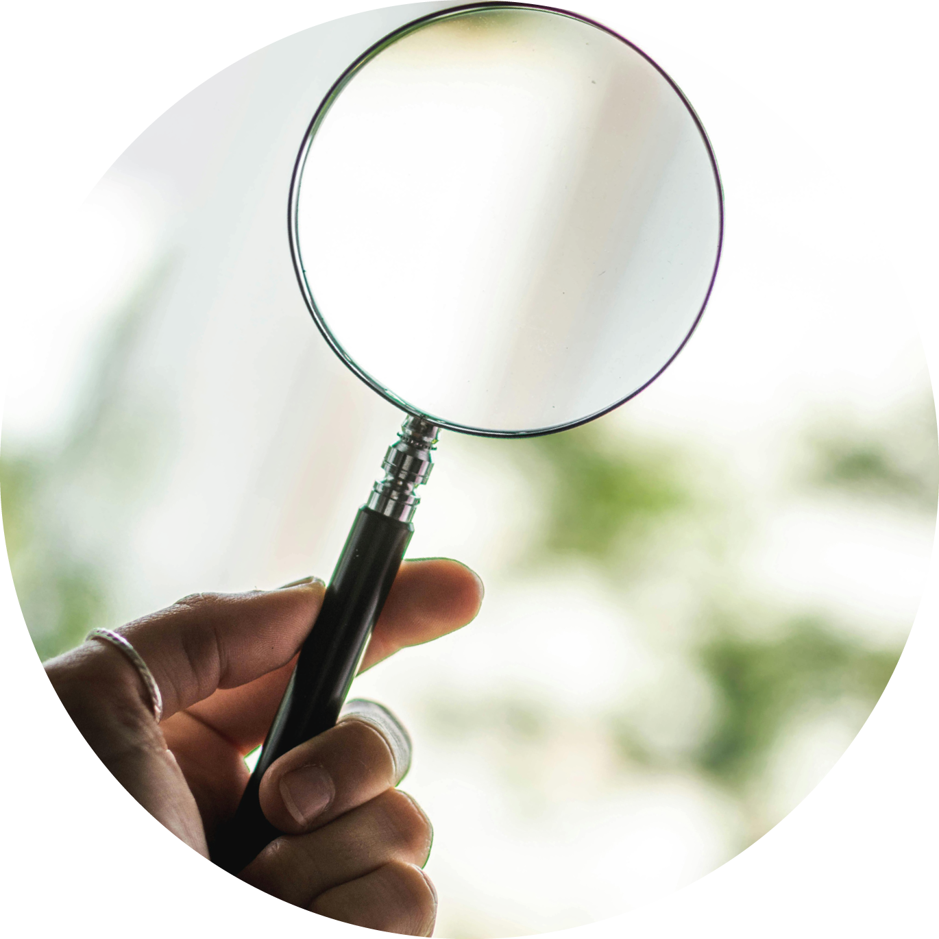 Eine Hand hält eine Lupe vor einem hellen, unscharfen Hintergrund.